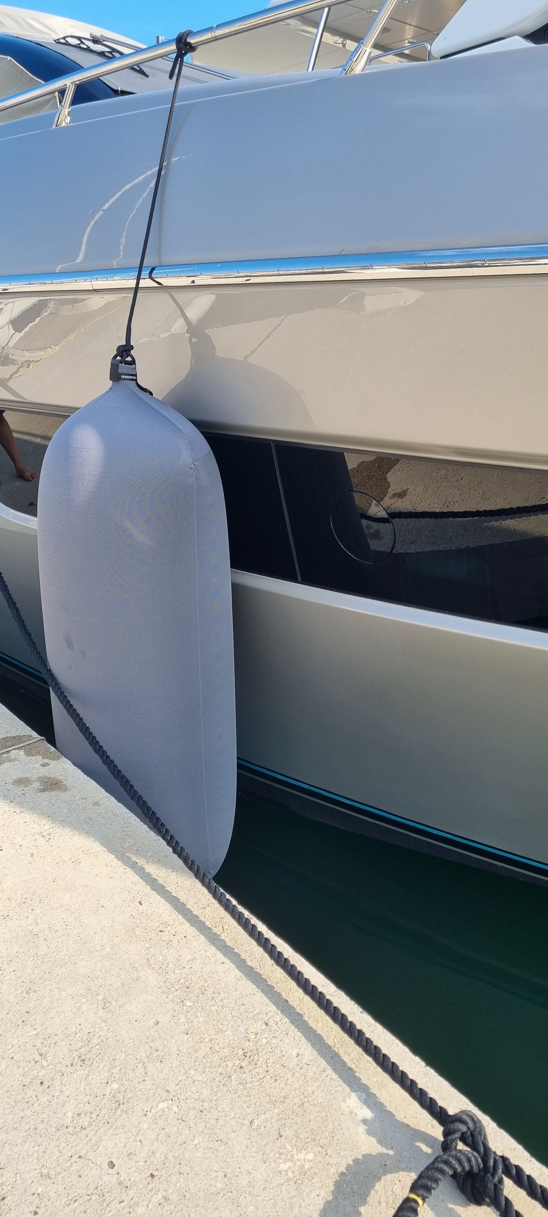 Close-up of a boat with a gray inflatable textile boat fender attached, docked at a pier.