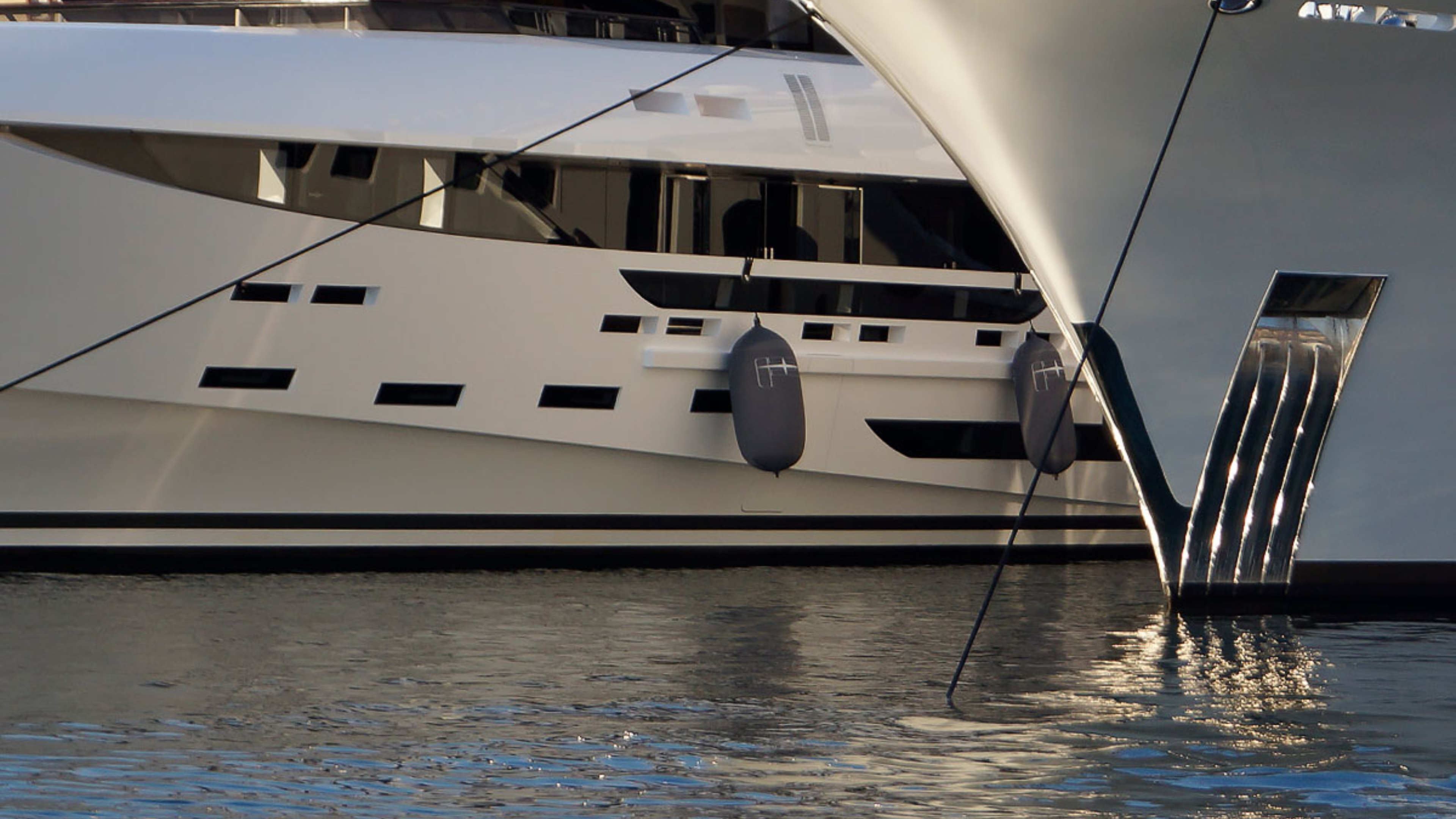 Close-up of a large white superyacht docked at a marina equipped with custom Fendertex boat fenders