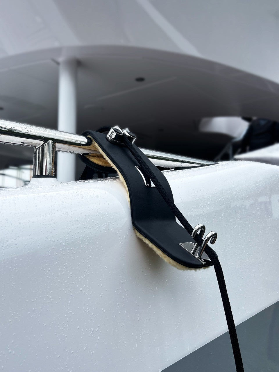 Close-up of a black leather fenderhook with metal clasps on a white hull of a superyacht.