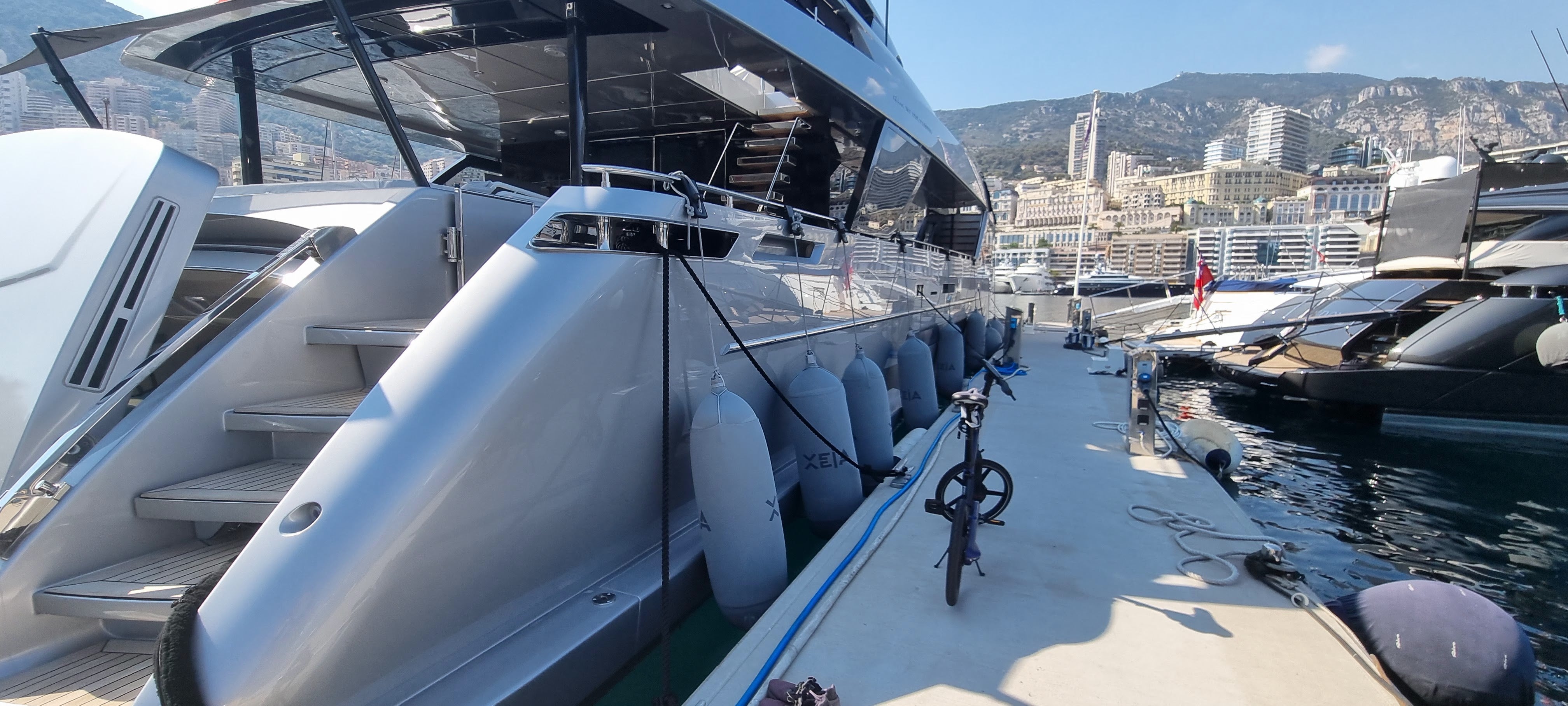 Luxury yacht docked at a marina with a cityscape in the background. Superyacht is equiped with durable textile fendertex boat fenders.